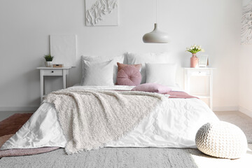 Cozy bed with white blanket and pillows in interior of light bedroom
