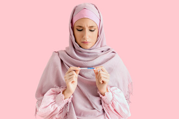 Troubled beautiful young woman in hijab with pregnancy test on pink background