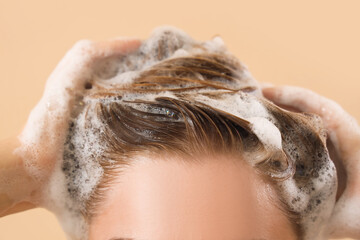 Naklejka premium Young woman washing hair on beige background, closeup