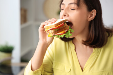Beautiful young woman eating tasty sandwich in kitchen, closeup