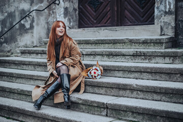 A stylish lady sitting on a vintage stairs outside with flowers.