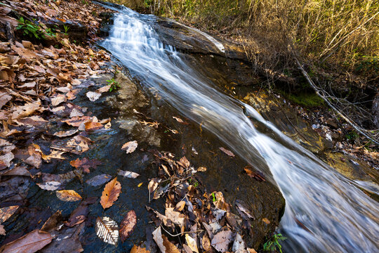 A thin waterfall cascades down a stone slope with autumn leaves in the foreground