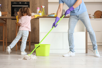 Cute little girl with her dad cleaning in kitchen - obrazy, fototapety, plakaty