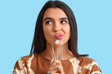 Thoughtful young woman with dental tools on blue background, closeup