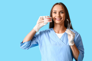 Smiling female dentist with jaw model and tools on blue background