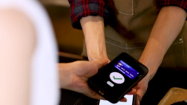 Closeup customer hand hold mobilephone making cashless payment in retails small business cafe coffee restaurant shop, cashier using qr code billing credit card, contactless online wireless application