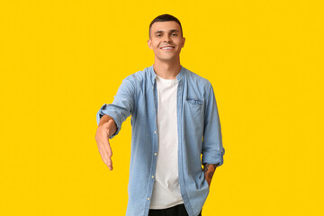 Handsome young man extending hand for handshake on yellow background - obrazy, fototapety, plakaty