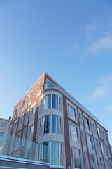 Obraz premium Looking up to red, pink brick new modern building towards light blue sky in Kalamaja. Tallinn, Estonia, Europe. January 2024.