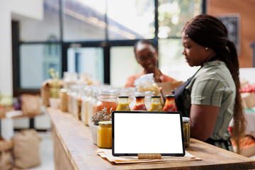 White screened tablet is set up on the counter to give vendors space to advertise eco-friendly products. Digital device at an eco-friendly store showing an isolated chromakey mockup template.
