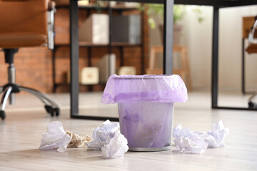 Overfilled trash bin with crumpled papers on floor in office, closeup
