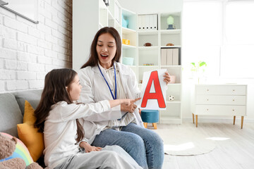 Female Asian speech therapist with little girl pronouncing letter A in office