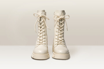 Pair of stylish white boots for women on light gray background. Trendy military beige boots on high platform with laces. Female fashion and shoes still life. Front view