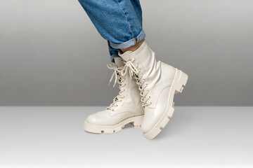Female legs in white combat boots and blue jeans stand on white background, side view. Woman...