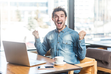 Portrait of cheerful happy positive young man freelancer in blue jeans shirt working on laptop,...