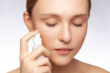 Closeup portrait of beautiful woman applying new skin care lotion on face to make face soft fresh...