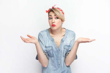 Portrait of puzzled confused young blonde woman wearing blue denim shirt and red headband standing...