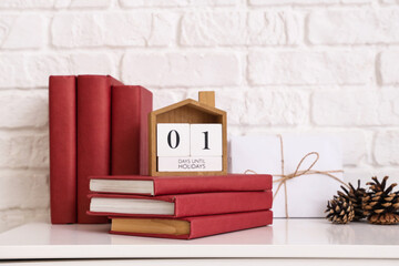 Books, cube calendar and pine cones on chest of drawers near white brick wall, closeup
