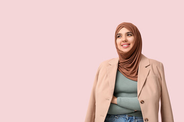 Happy young Muslim woman in hijab on pink background