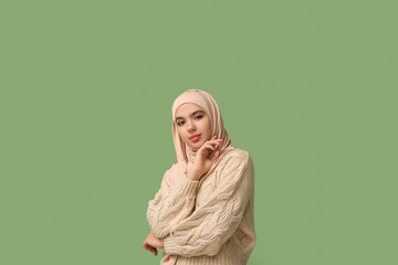 Fototapeta premium Pretty young Muslim woman in hijab on green background