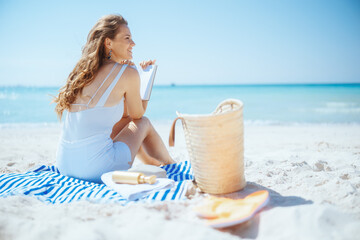 smiling stylish woman on beach with straw bag and book