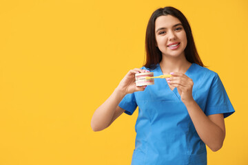 Female dentist with jaw model and toothbrush on yellow background. World Dentist Day