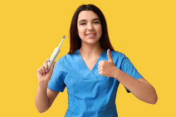 Female dentist with electric toothbrush showing thumb-up gesture on yellow background. World Dentist Day