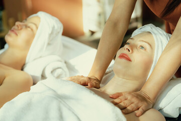 Obraz na płótnie Canvas A portrait of two beautiful woman having back massage by professional masseur and falling in deep relaxation surrounded by traditional spa environment. Calming and relaxing concept. Tranquility.