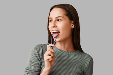 Beautiful young woman with tongue scraper on grey background