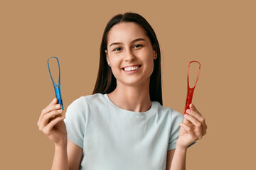 Beautiful young woman with tongue scrapers on brown background