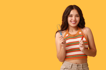 Happy young Asian woman with tongue scrapers on yellow background