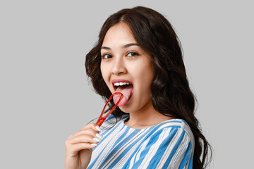 Young Asian woman with tongue scraper on grey background - obrazy, fototapety, plakaty