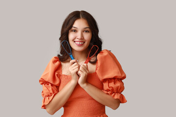 Happy young Asian woman with tongue scrapers on grey background