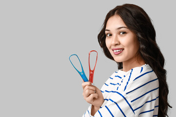Young Asian woman with tongue scrapers on grey background
