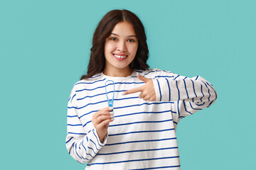 Young Asian woman pointing at tongue scraper on blue background