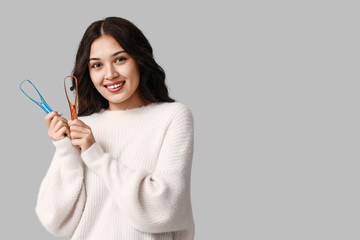 Happy young Asian woman with tongue scrapers on grey background