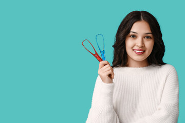 Happy young Asian woman with tongue scrapers on blue background