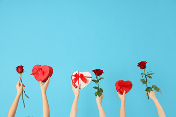 Female hands holding heart-shaped gift boxes and roses on blue background. Valentine's Day...