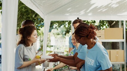 Young African American and Caucasian volunteers handing out free food and necessities to the less...