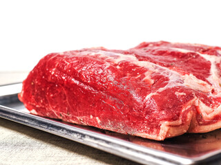 Uncooked strip loin joint on metal tray and on white background. Raw high quality and price piece of beef meat.