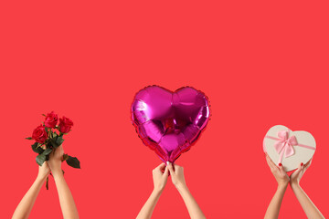 Female hands holding heart-shaped balloon, gift box and roses on red background. Valentine's Day celebration