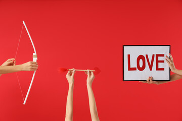Female hands holding frame with word LOVE, Cupid's bow and arrow on red background. Valentine's Day...