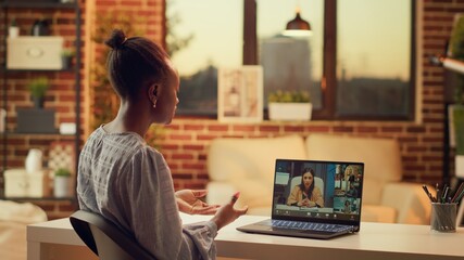 Worker chatting with clients on videocall, talking about price list and services to build online career in freelancing job. Woman using teleconference remote call at home, sunset light.