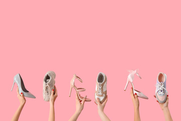 Female hands holding stylish high heeled shoes and sneakers on pink background