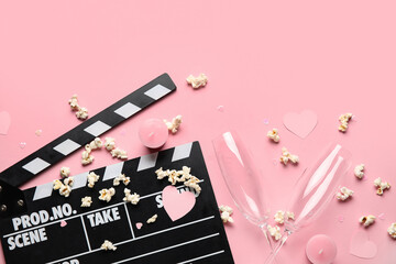 Movie clapper with champagne glasses, popcorn and candles on pink background. Valentine's Day...
