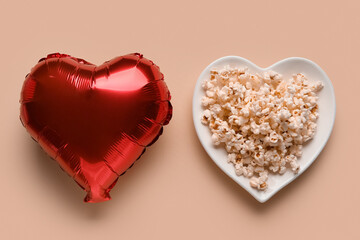 Plate with popcorn and heart shaped balloon on beige background. Valentine's Day celebration