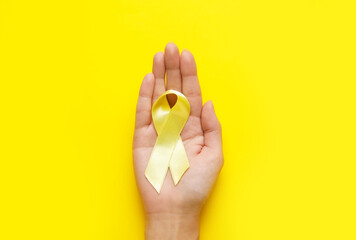 Female hands with golden awareness ribbon on yellow background. International Childhood Cancer Day