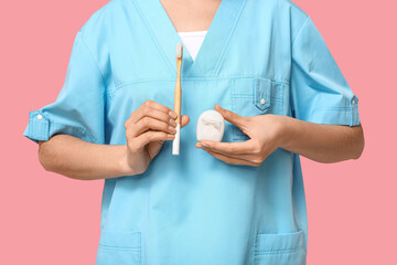 Female dentist with dental floss and toothbrush on pink background