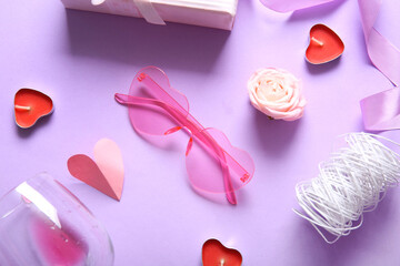 Pink heart shaped sunglasses with glass, candles and decor on lilac background. Valentine's Day concept