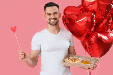 Young man with tasty breakfast and heart-shaped balloons on pink background. Valentine's Day celebration