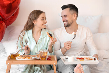 Happy young couple having breakfast in bed on Valentine's Day